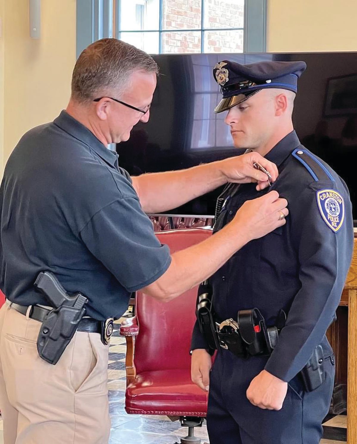 FATHER AND SON: Coventry Police Detective Sgt. Kevin Nolan pins the badge on his son, newly sworn-in Cranston Police Officer Michael Nolan, during last week’s ceremony